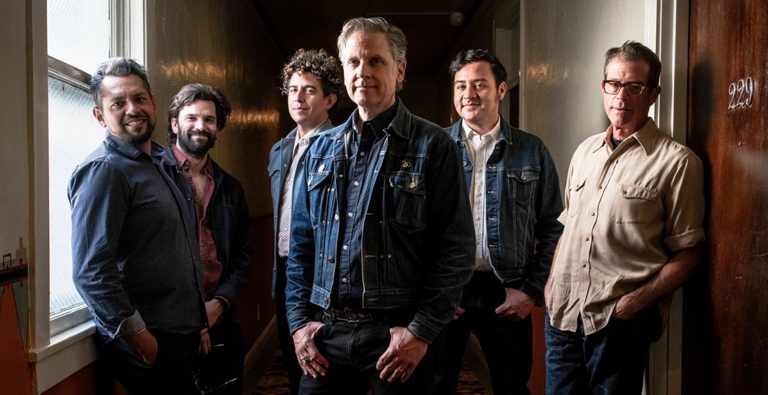 six members of the band Calexico stand staggered in a hallway
